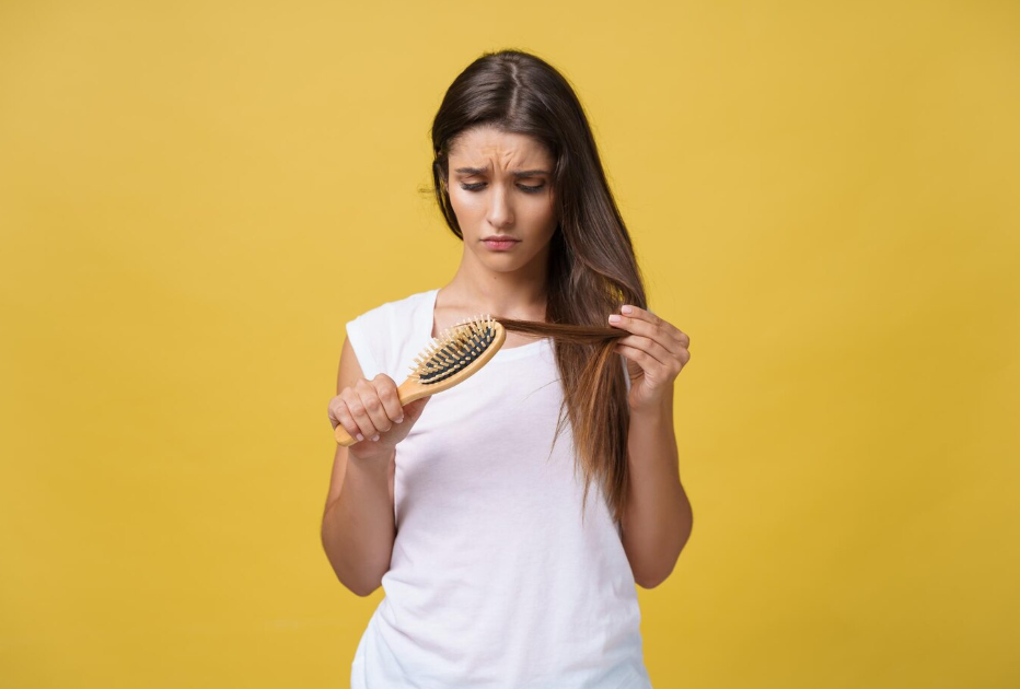 A woman gently combs through her damaged hair, trying to smooth out the tangles.