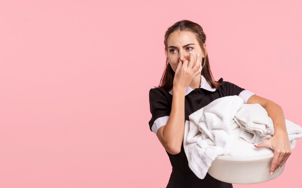 A woman holding clothes with an unpleasant odor.